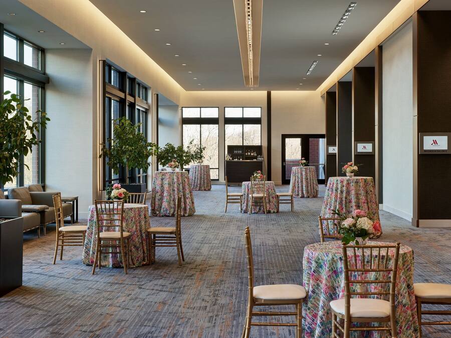 A spacious hotel lobby with round tables covered in floral tablecloths, comfortable seating, and large windows allowing natural light.