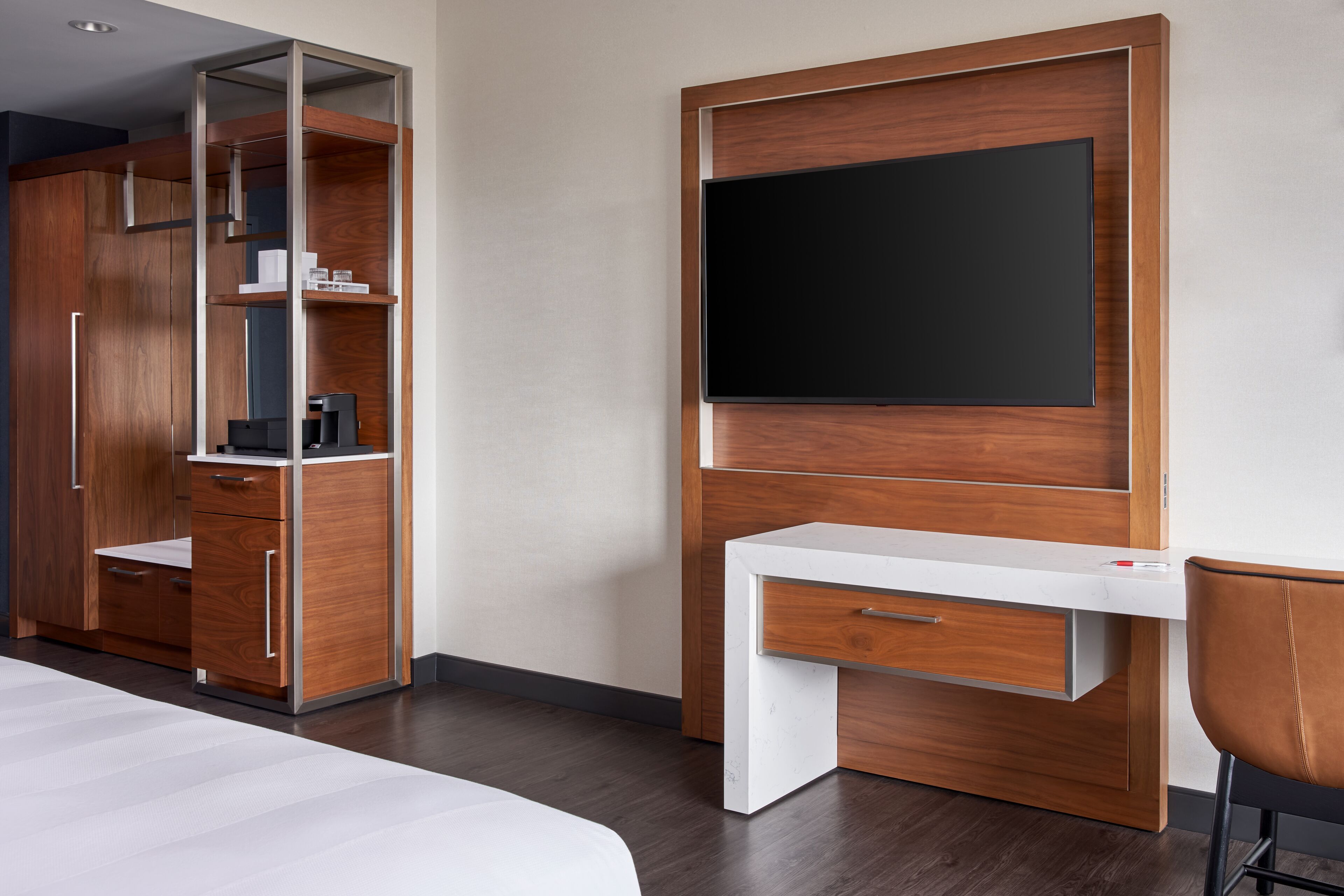 A modern hotel room with a wooden wardrobe, a desk with a flat-screen TV, and a single chair.