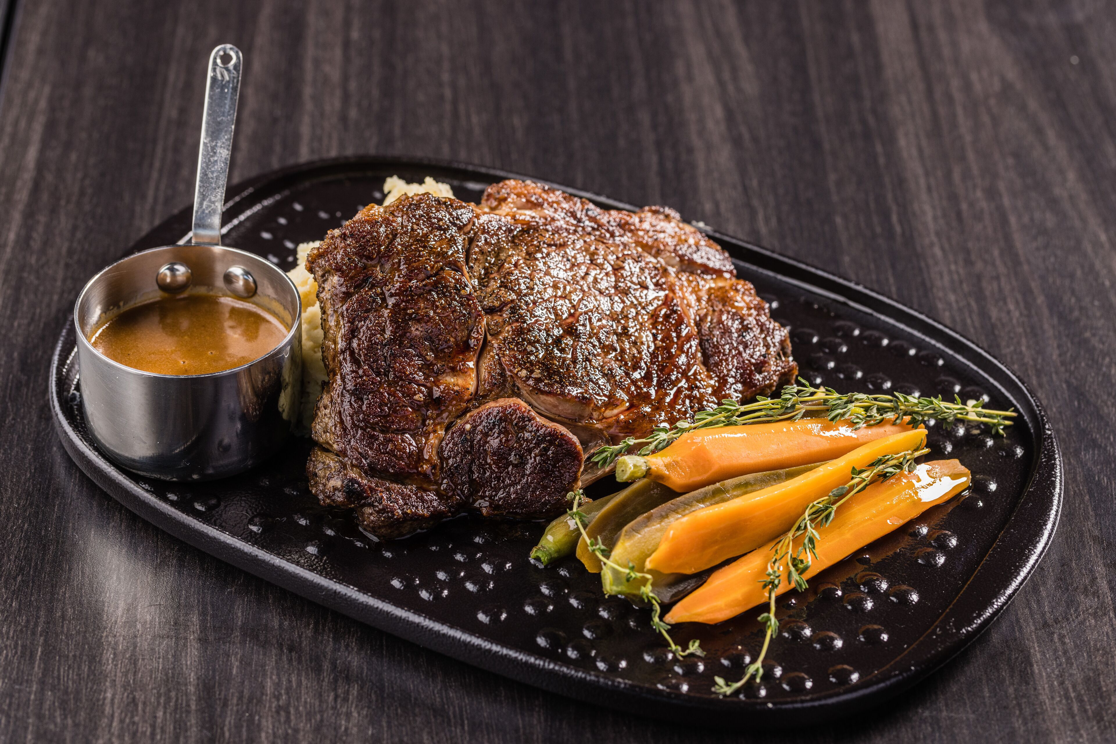 Un bistec con salsa de carne y zanahorias en un plato negro.