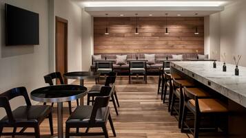 Un área de bar moderna con mesas redondas, taburetes de bar y una barra alargada.