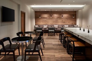 Un área de bar moderna con mesas redondas, taburetes de bar y una barra alargada.