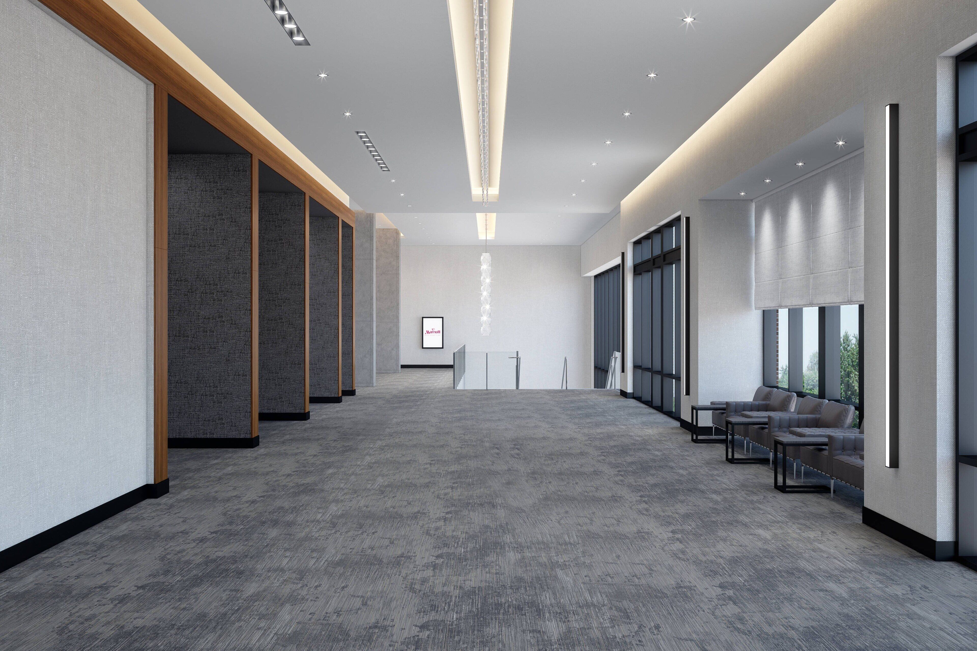 A spacious hallway with a grey carpet, wooden paneling on the left, and a seating area with sofas on the right.