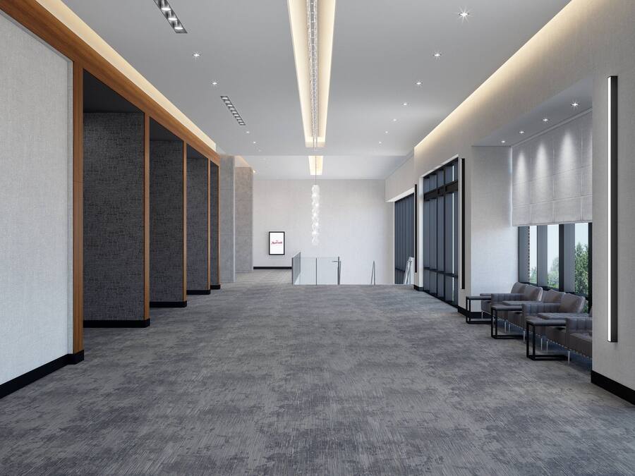 A spacious hallway with a grey carpet, wooden paneling on the left, and a seating area with sofas on the right.