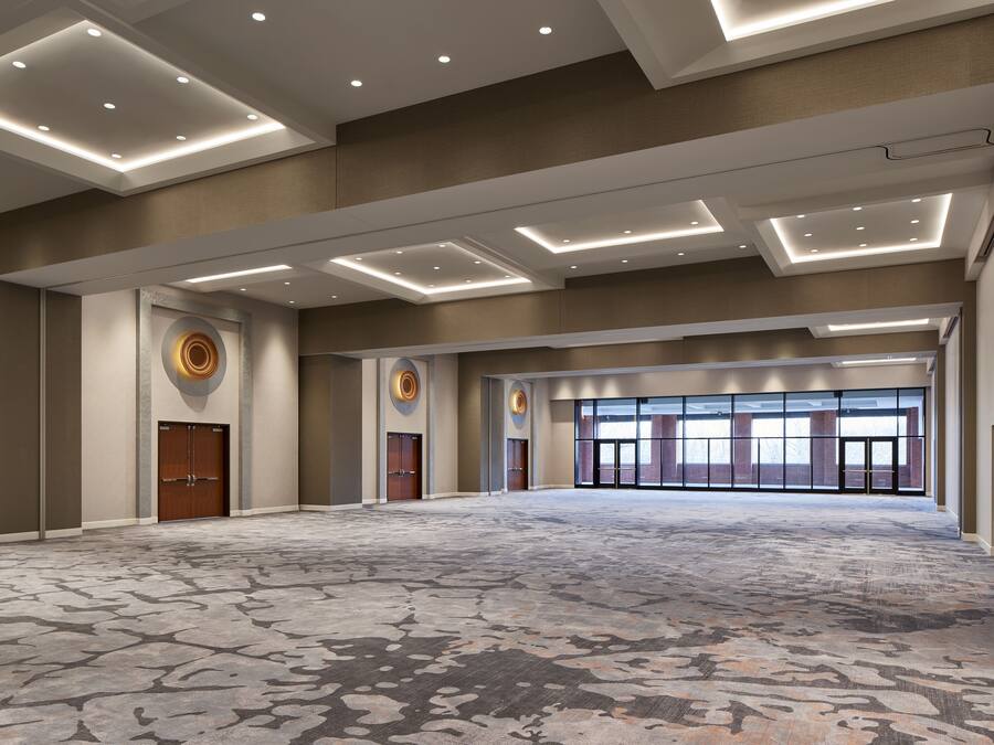 A spacious, well-lit conference room with a patterned carpet, recessed ceiling lights, and large windows.