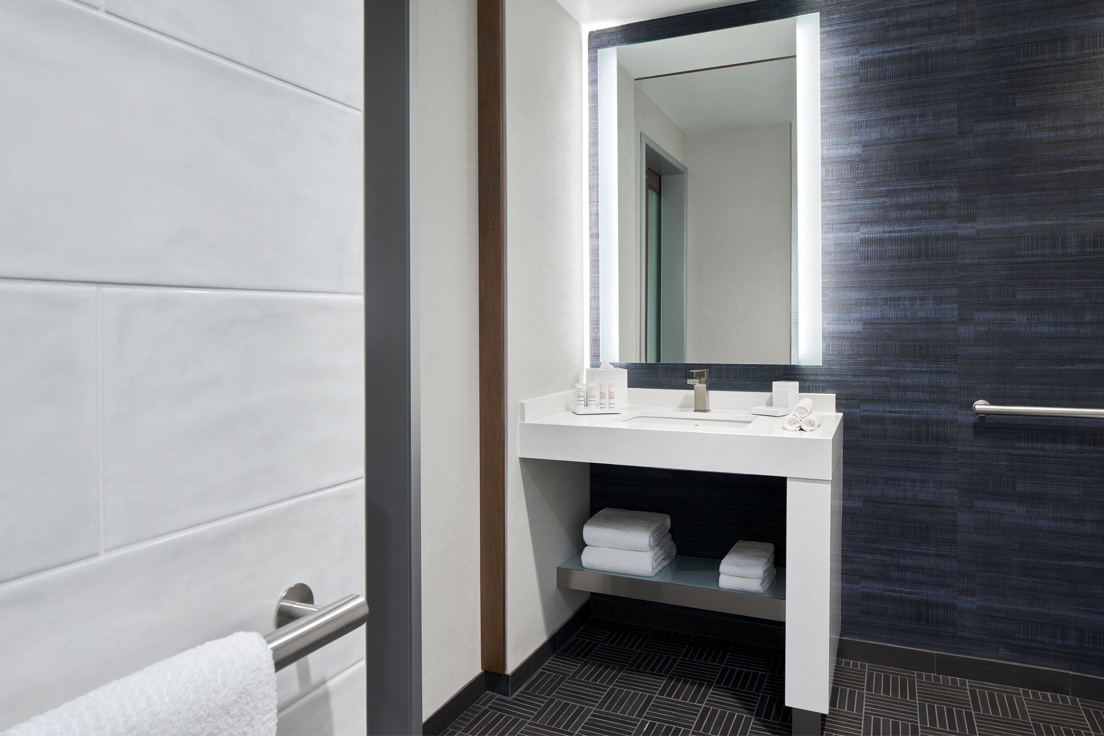 Un baño moderno con tocador blanco, un espejo grande y un perchero para toallas.