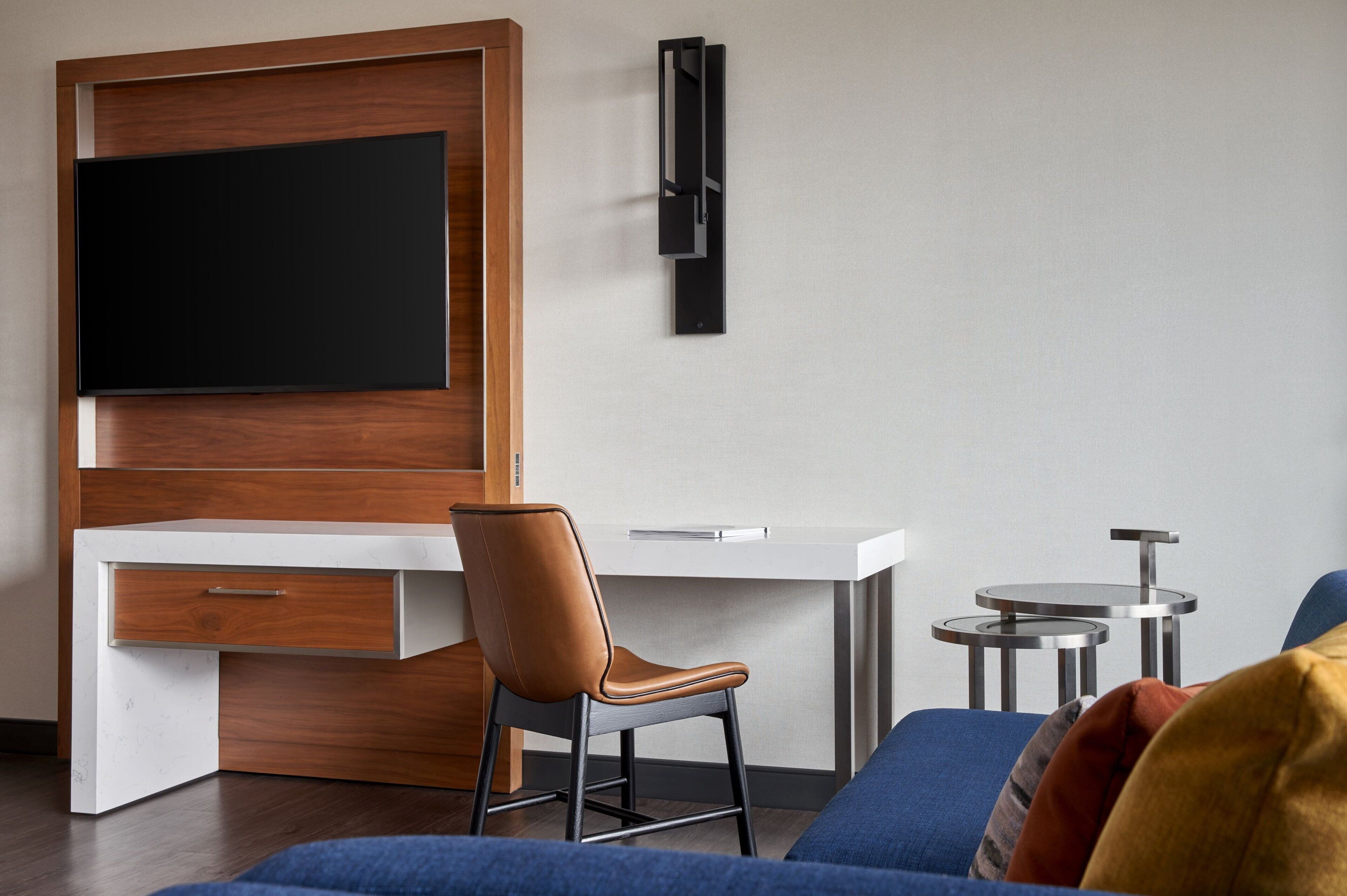 A modern room with a wooden desk, a TV mounted on the wall, a brown leather chair, and two small round tables.