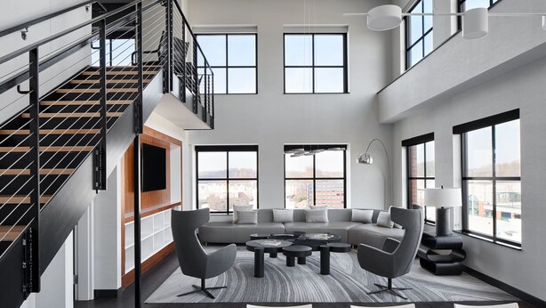 A spacious living area with a large sectional sofa, a coffee table, and a staircase with a railing. - Marriott Owings Mills Metro Centre (Owings Mills)