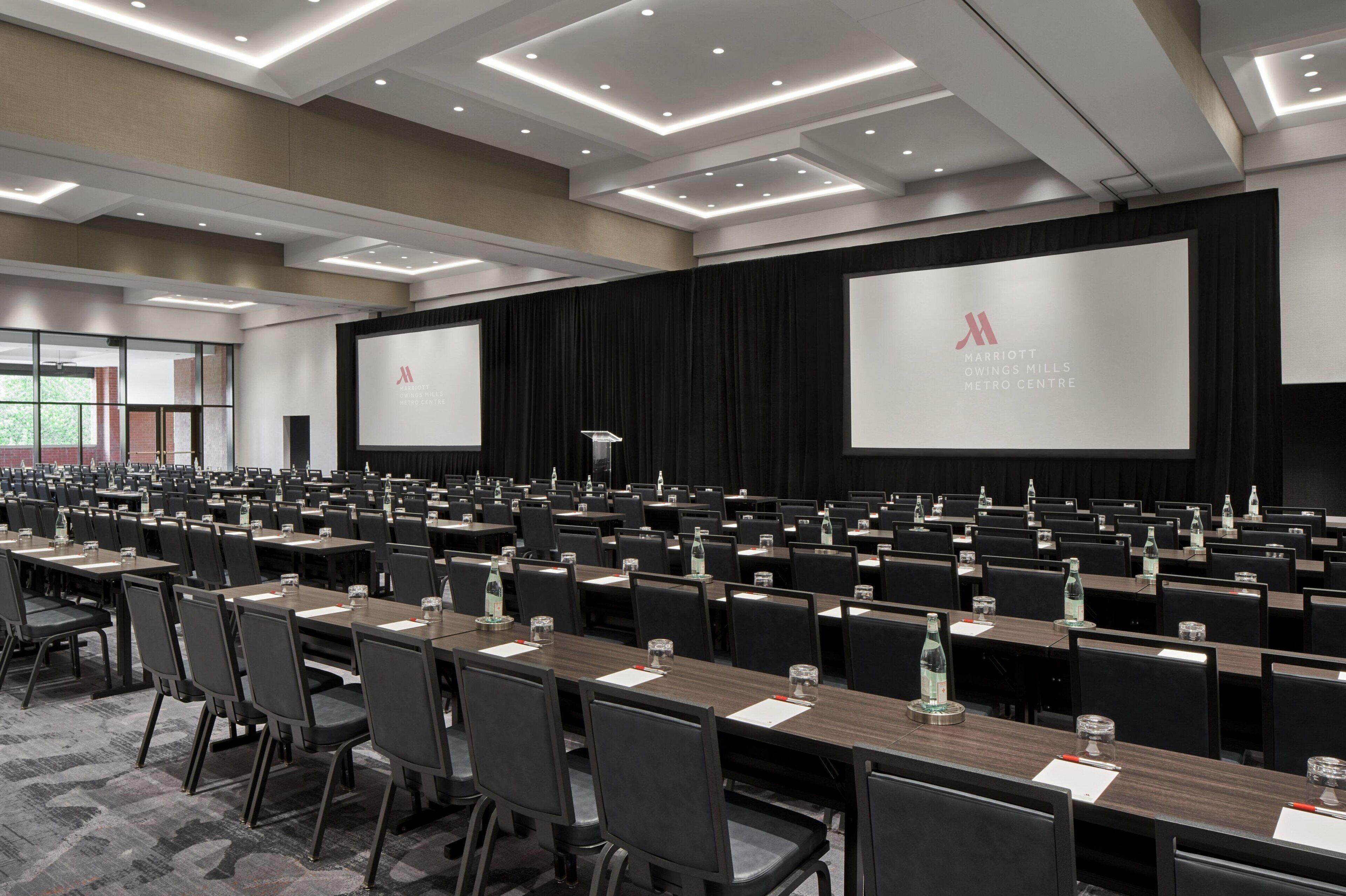 A conference room with rows of tables and chairs, a large screen, and a podium.