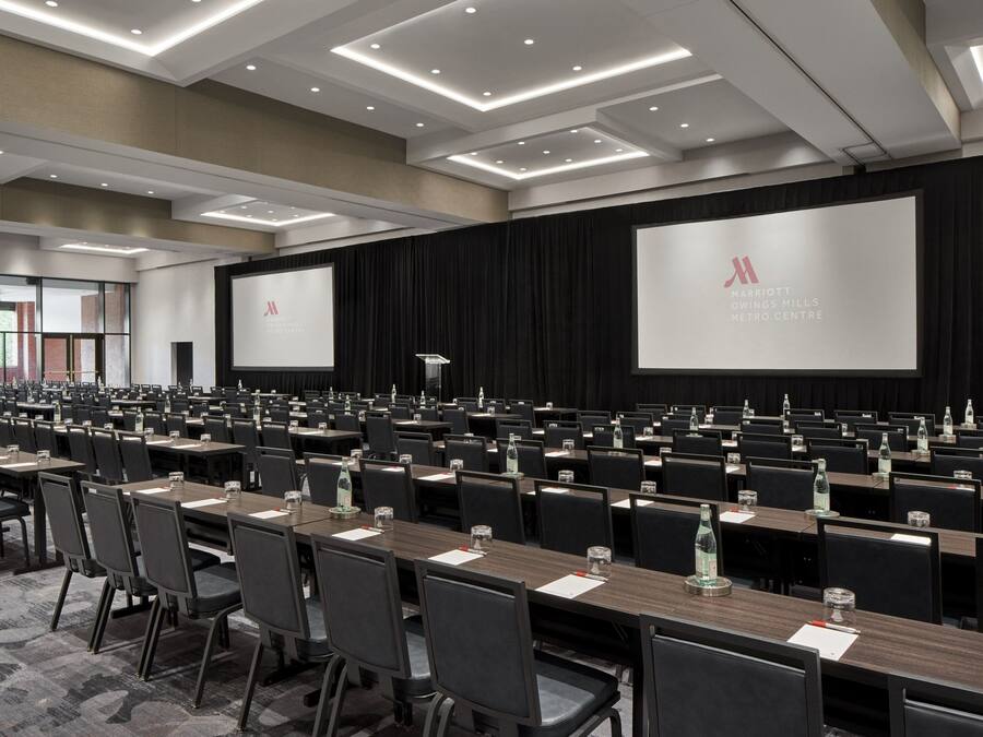 A conference room with rows of tables and chairs, a large screen, and a podium.