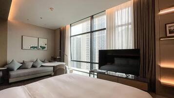 A modern hotel room with a large bed, a sofa, a TV, and a large window with curtains.
