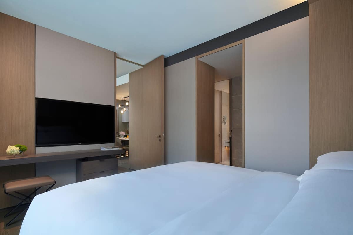 Habitación de hotel moderna con una cama grande, televisión de pantalla plana, escritorio con silla y un pequeño rincón de descanso.