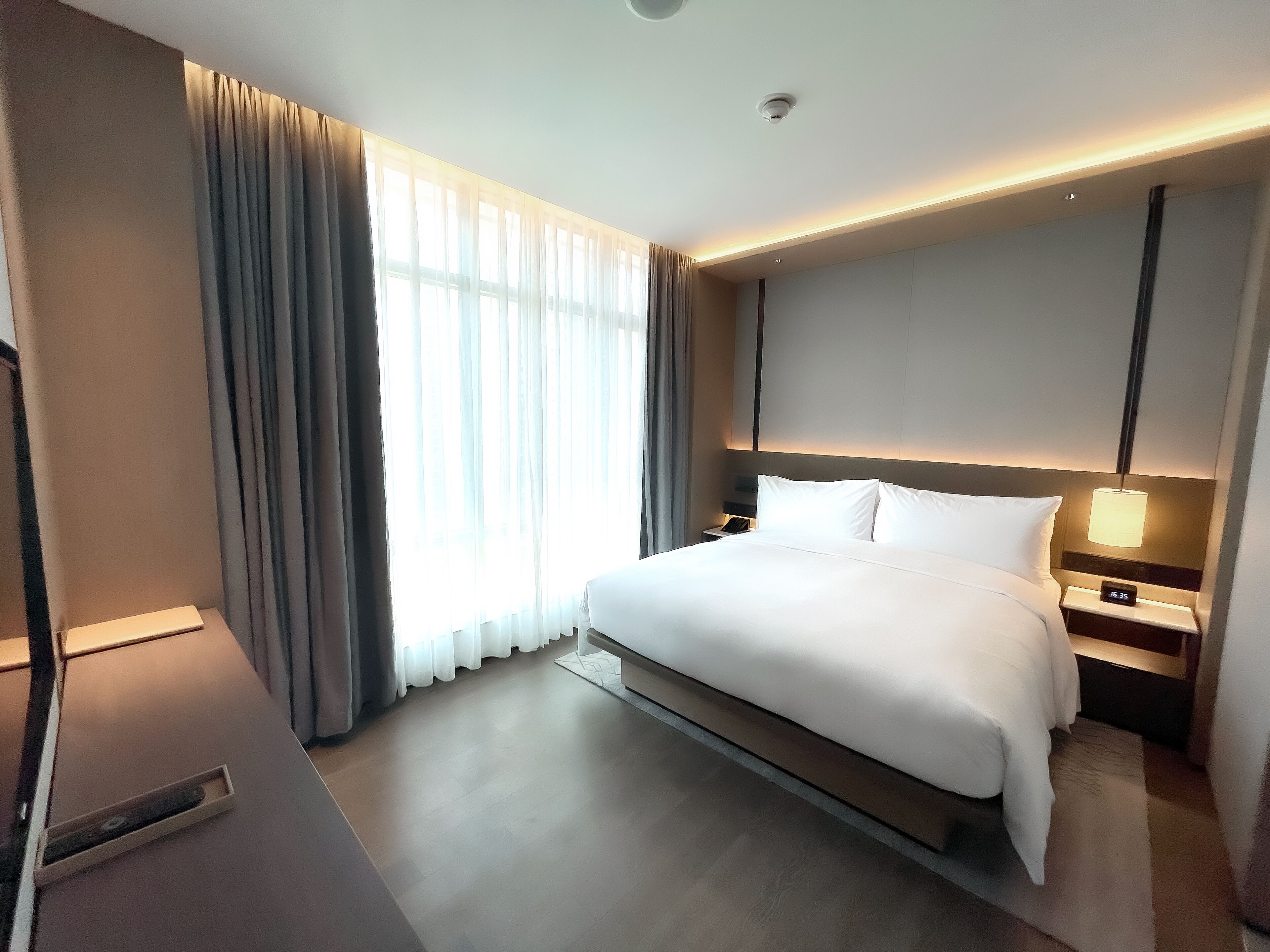 Ein modernes Hotelzimmer mit einem großen Bett, Nachttischen, einem Fenster mit Vorhängen.
