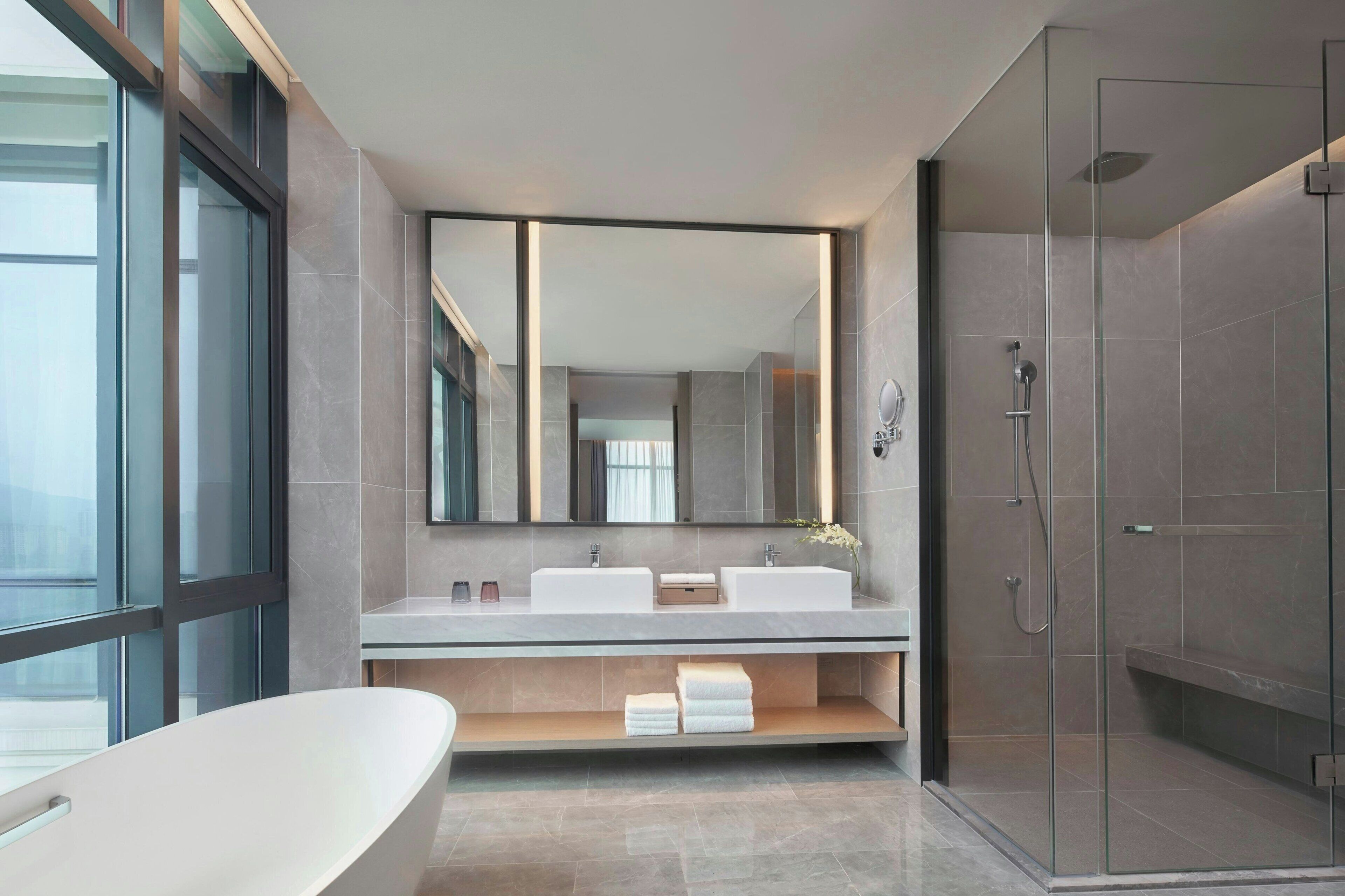 A modern bathroom with a large mirror, two sinks, a shower, and a bathtub.