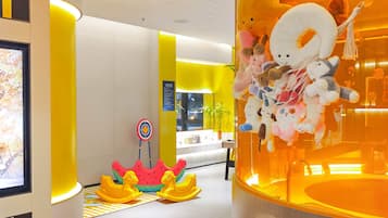 A brightly lit indoor space with a yellow and white color scheme, featuring a display of plush toys, a target board, and a children's play area with yellow rocking horses.