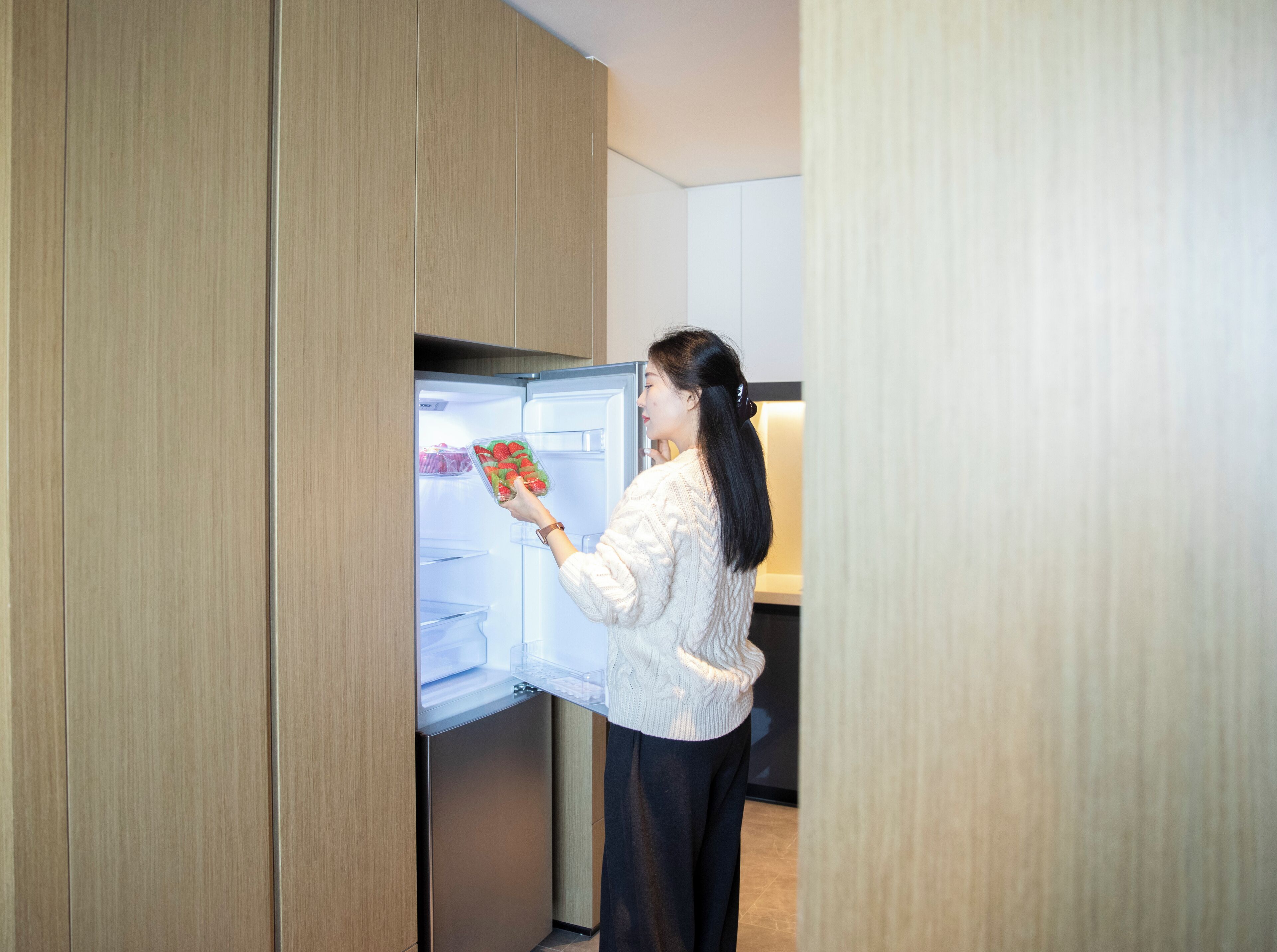 A person opening a modern refrigerator in a room with wooden paneling.
