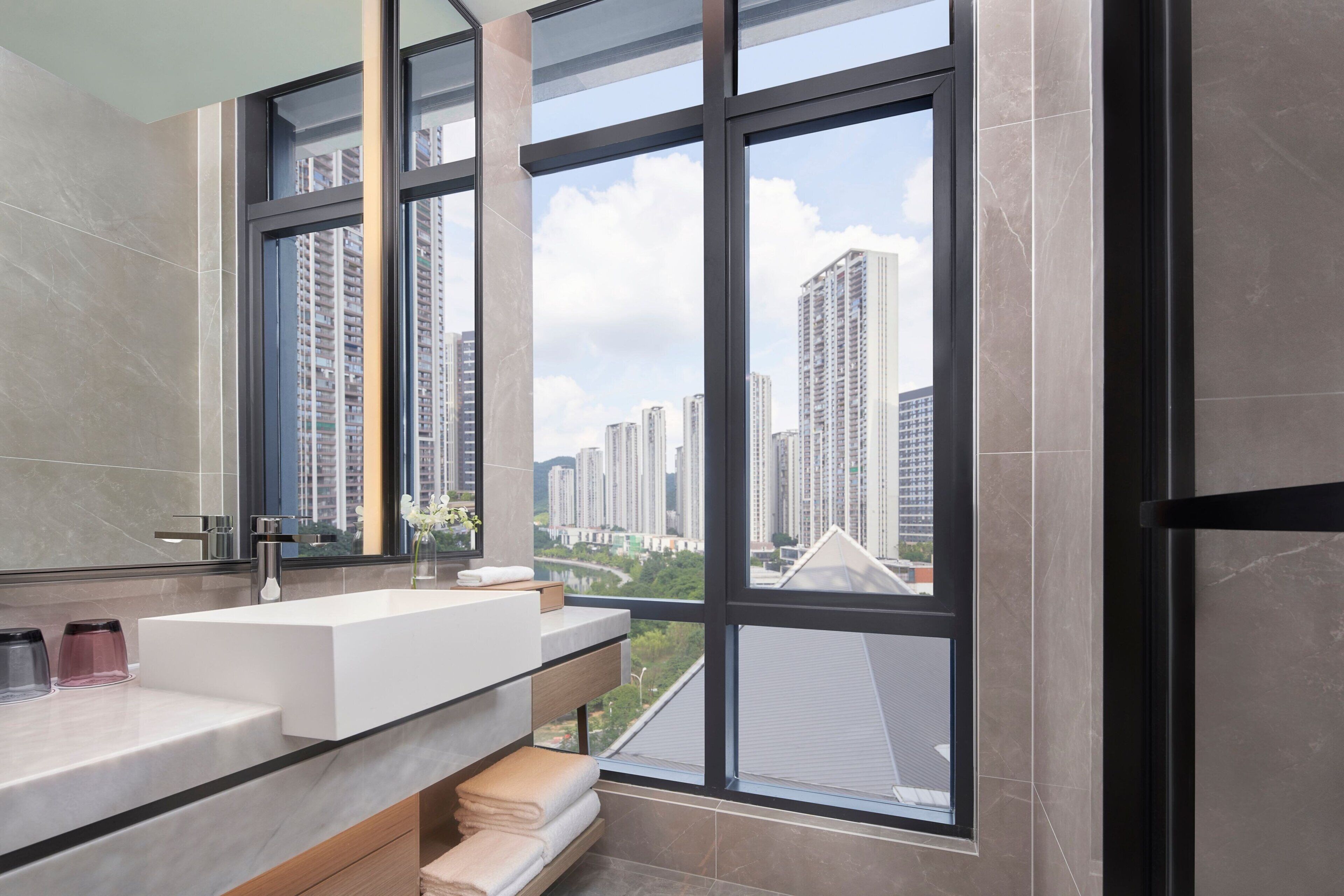 A modern bathroom with a large window, a white sink, and a mirror.