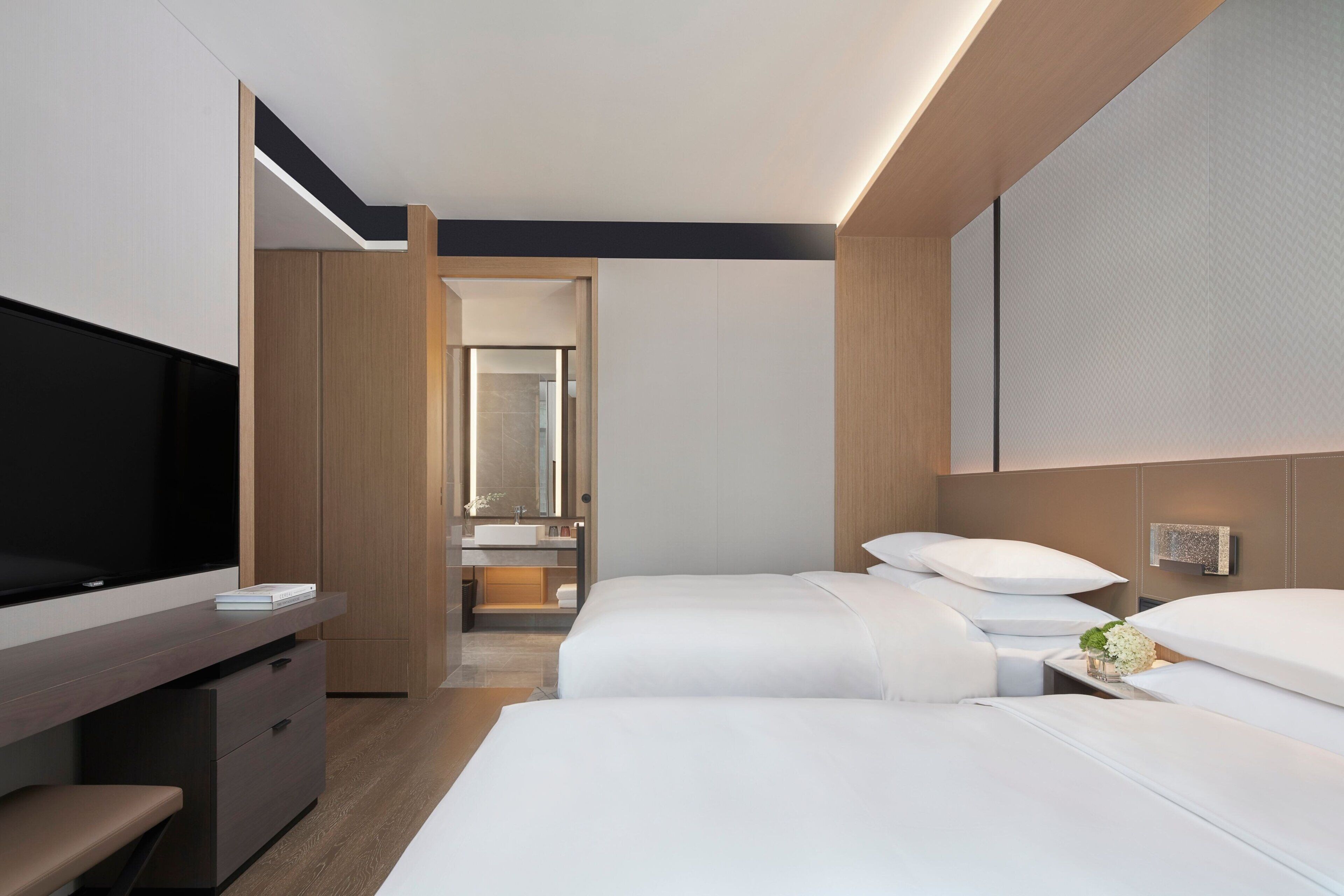 A hotel room with a bed, a TV, a desk, and a bathroom visible through an open door.