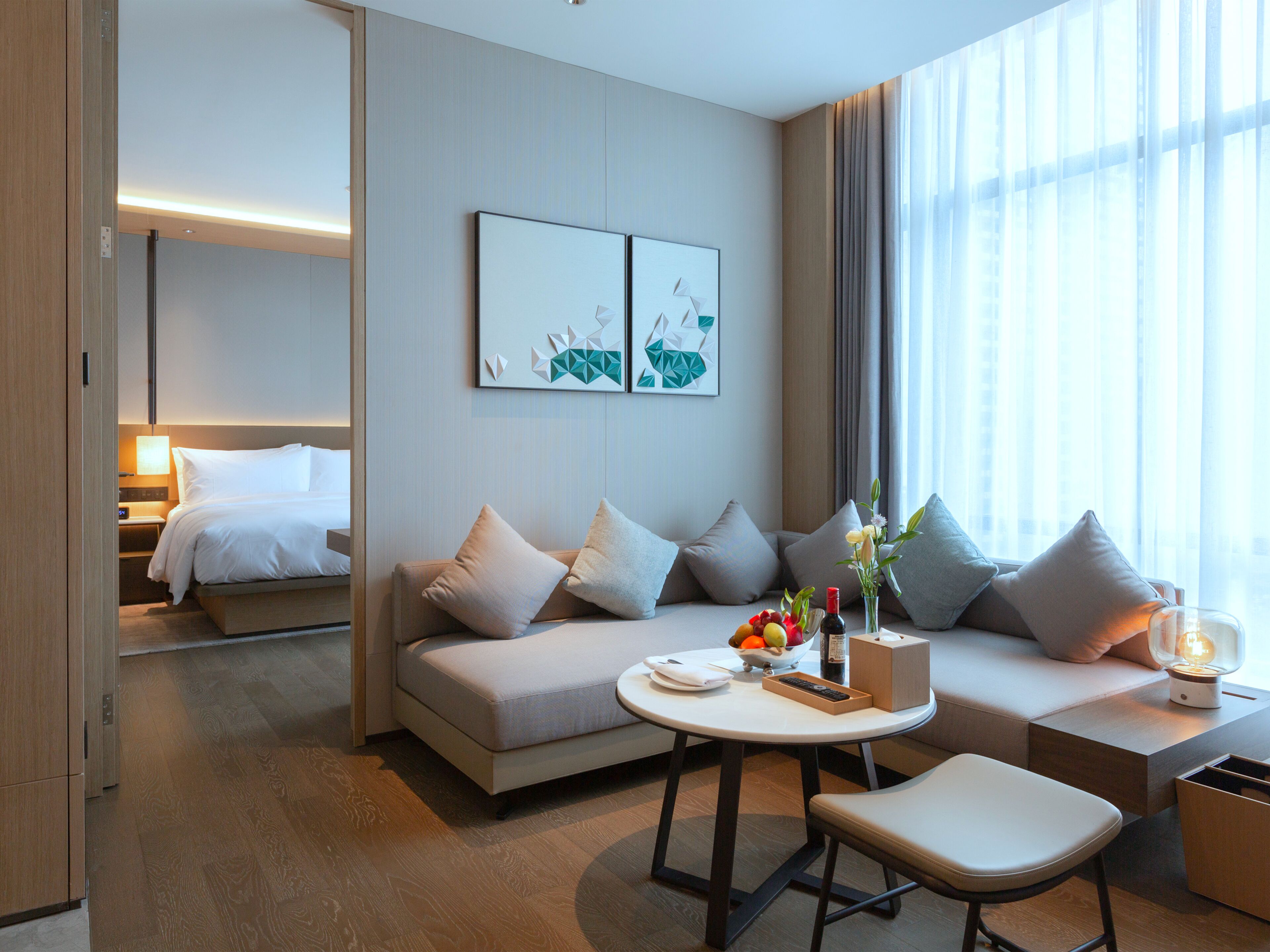 Une chambre d’hôtel moderne avec un canapé, une petite table sur laquelle se trouve un panier de fruits, et un lit en arrière-plan.