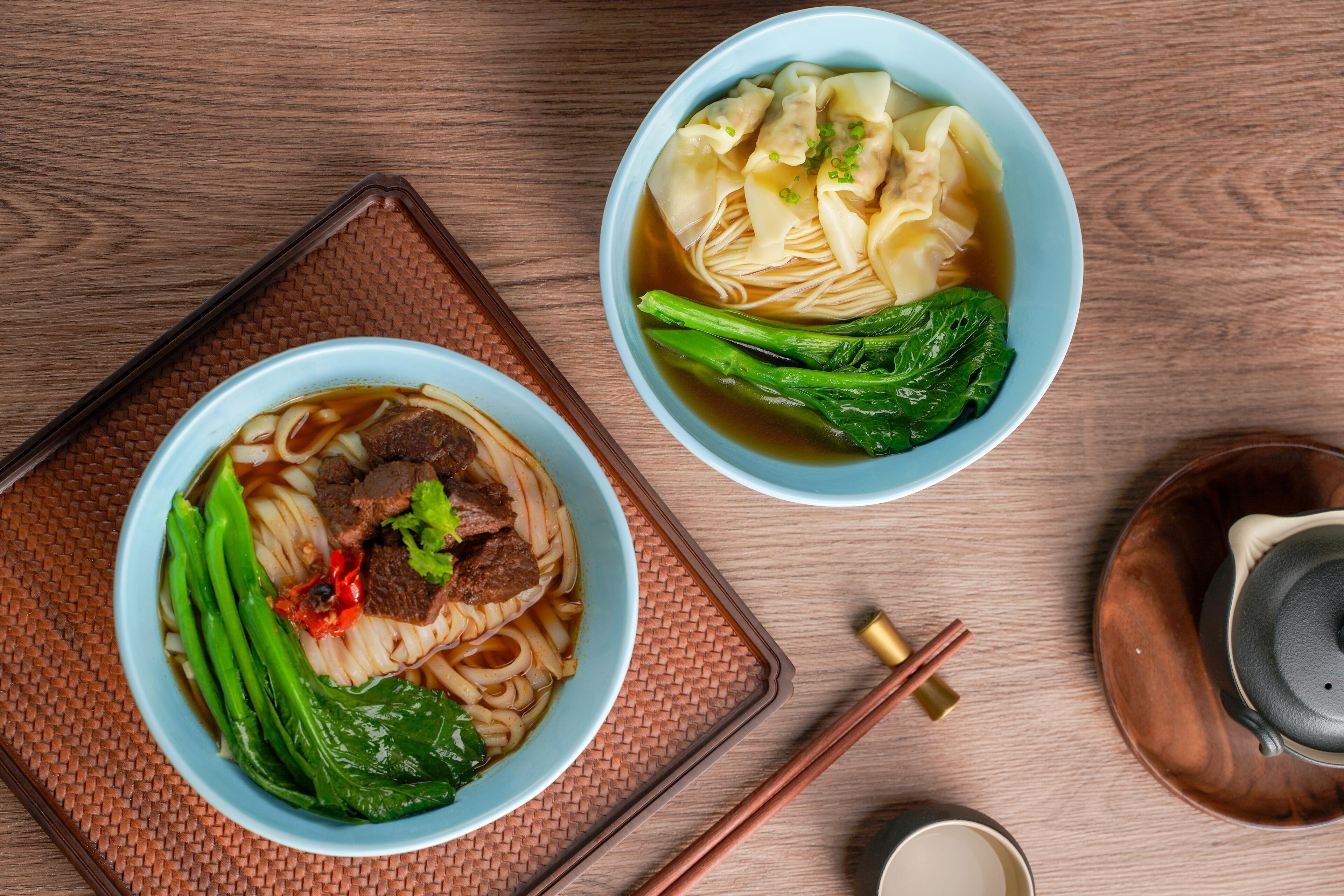 Dos tazones de sopa de fideos con carne y verduras sobre una mesa de madera.