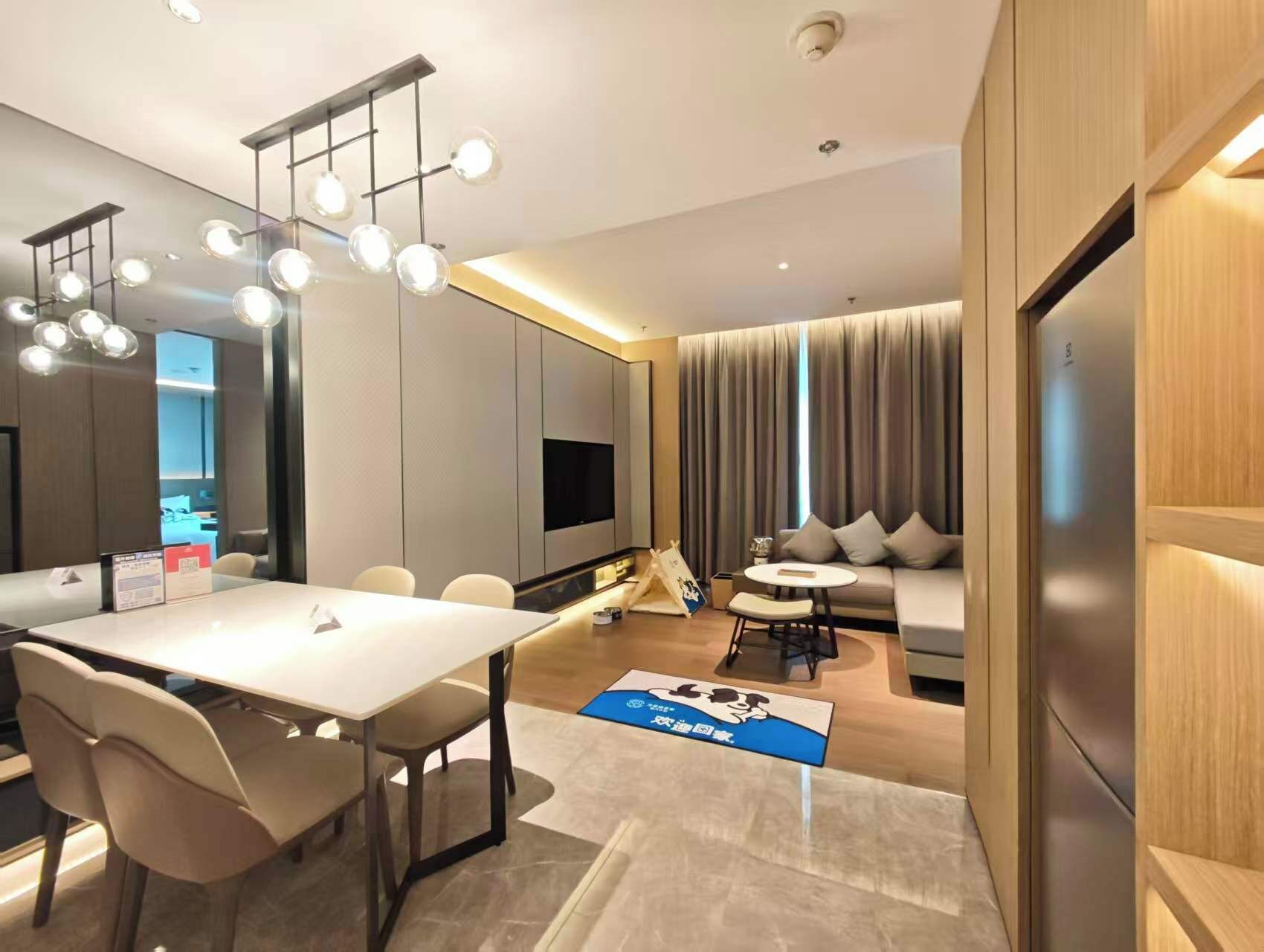 A modern hotel room with a dining area, a sofa, a TV, and a large window with curtains.