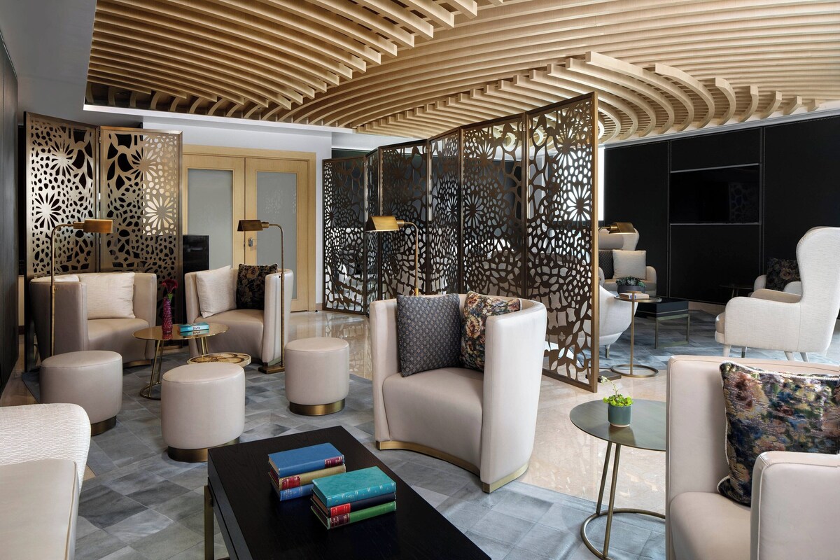 A modern hotel lobby with a curved ceiling, plush seating, and decorative screens.