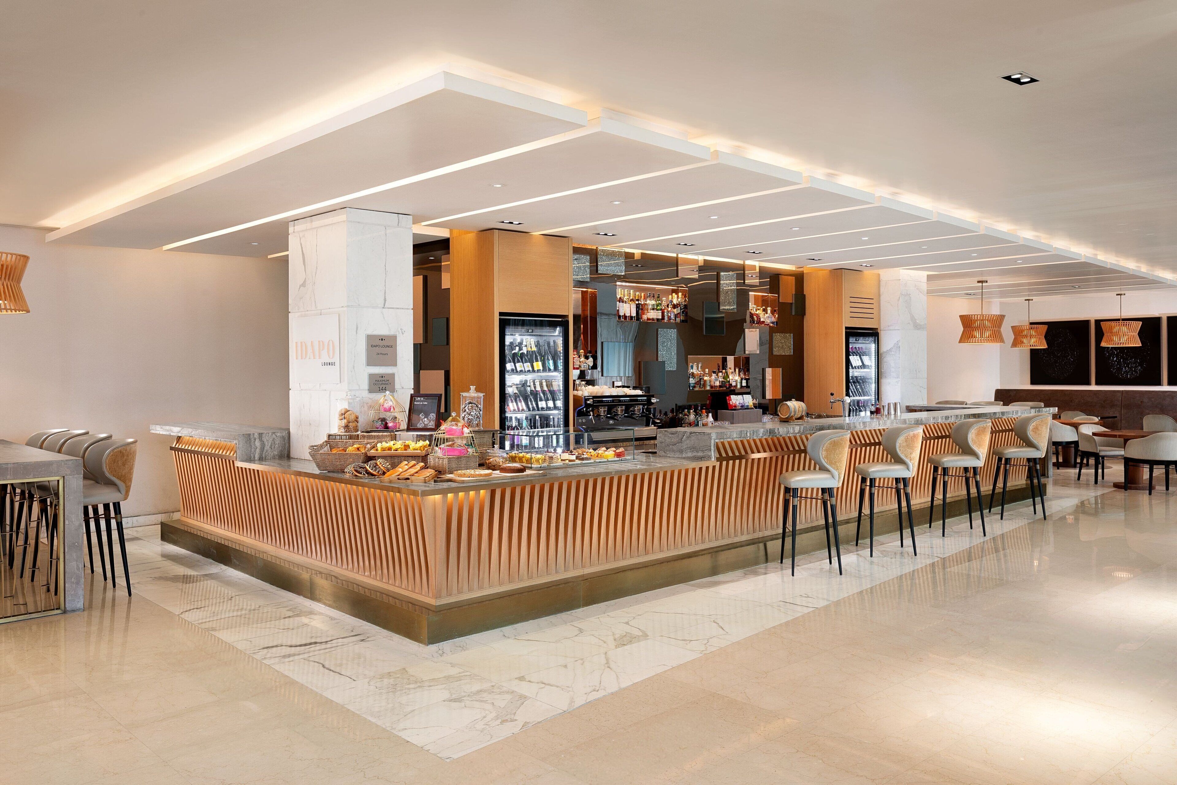 Un moderno bar con barra central, taburetes y una zona de estar con mesas y sillas.