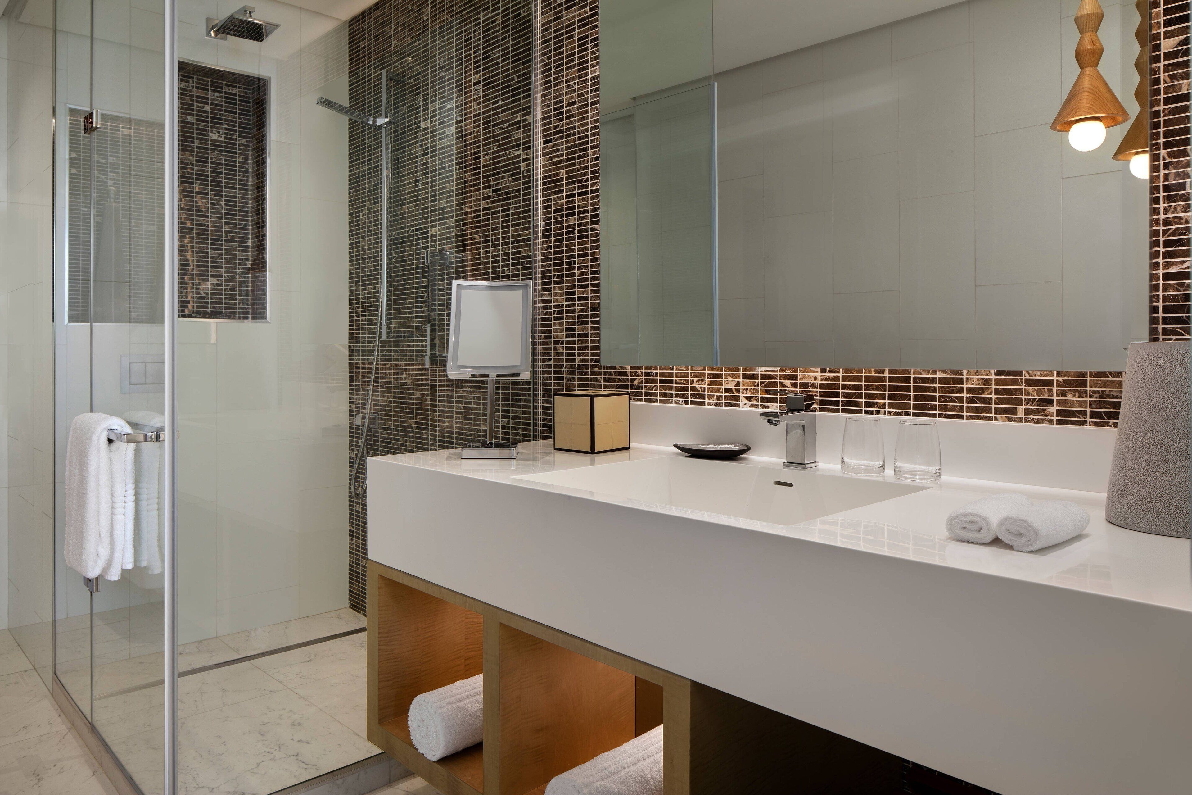 A modern bathroom with a glass shower enclosure, a white sink, and a large mirror.