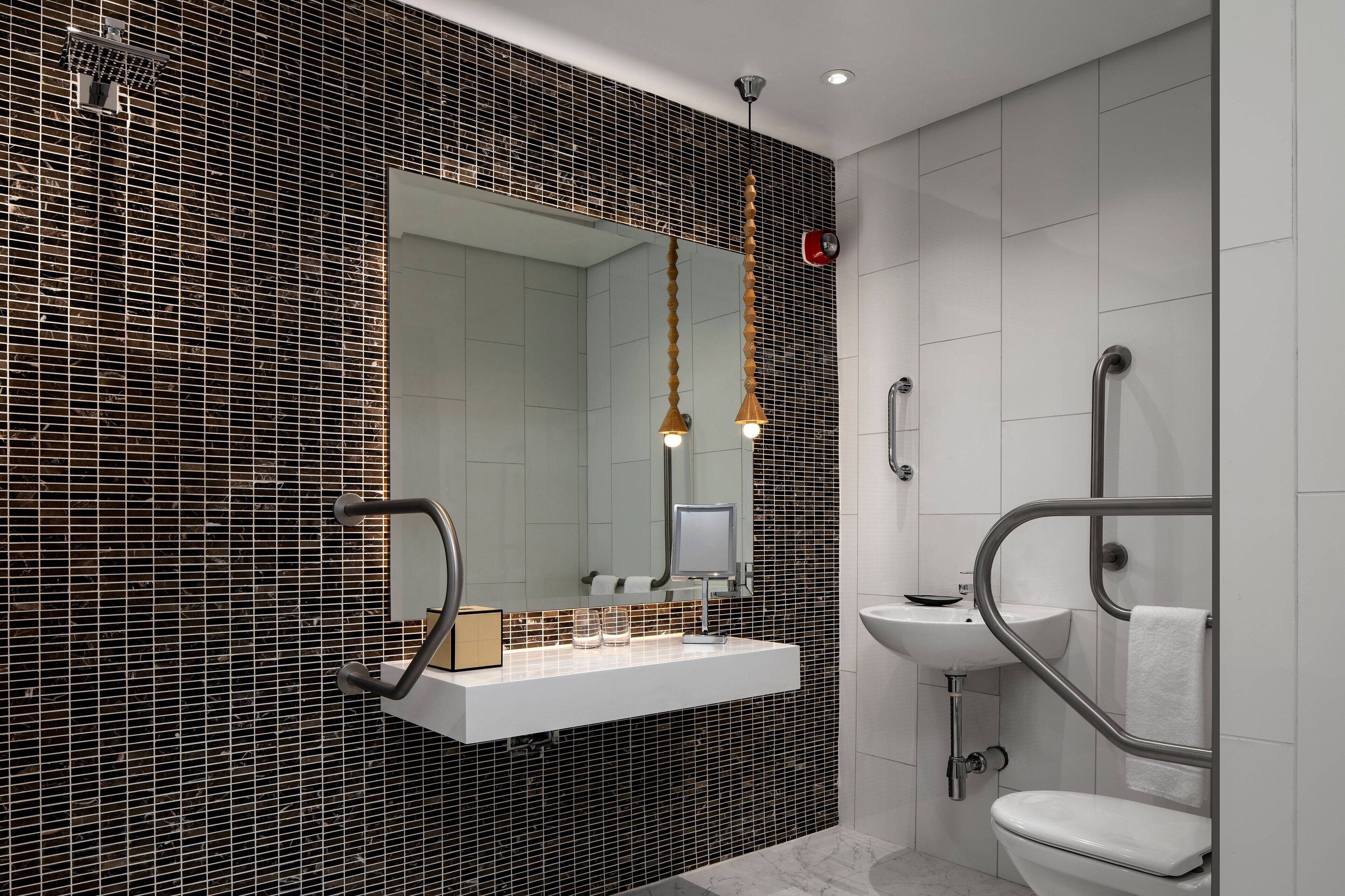 A modern bathroom with a black tiled backsplash, a white vanity, a mirror, and a toilet.