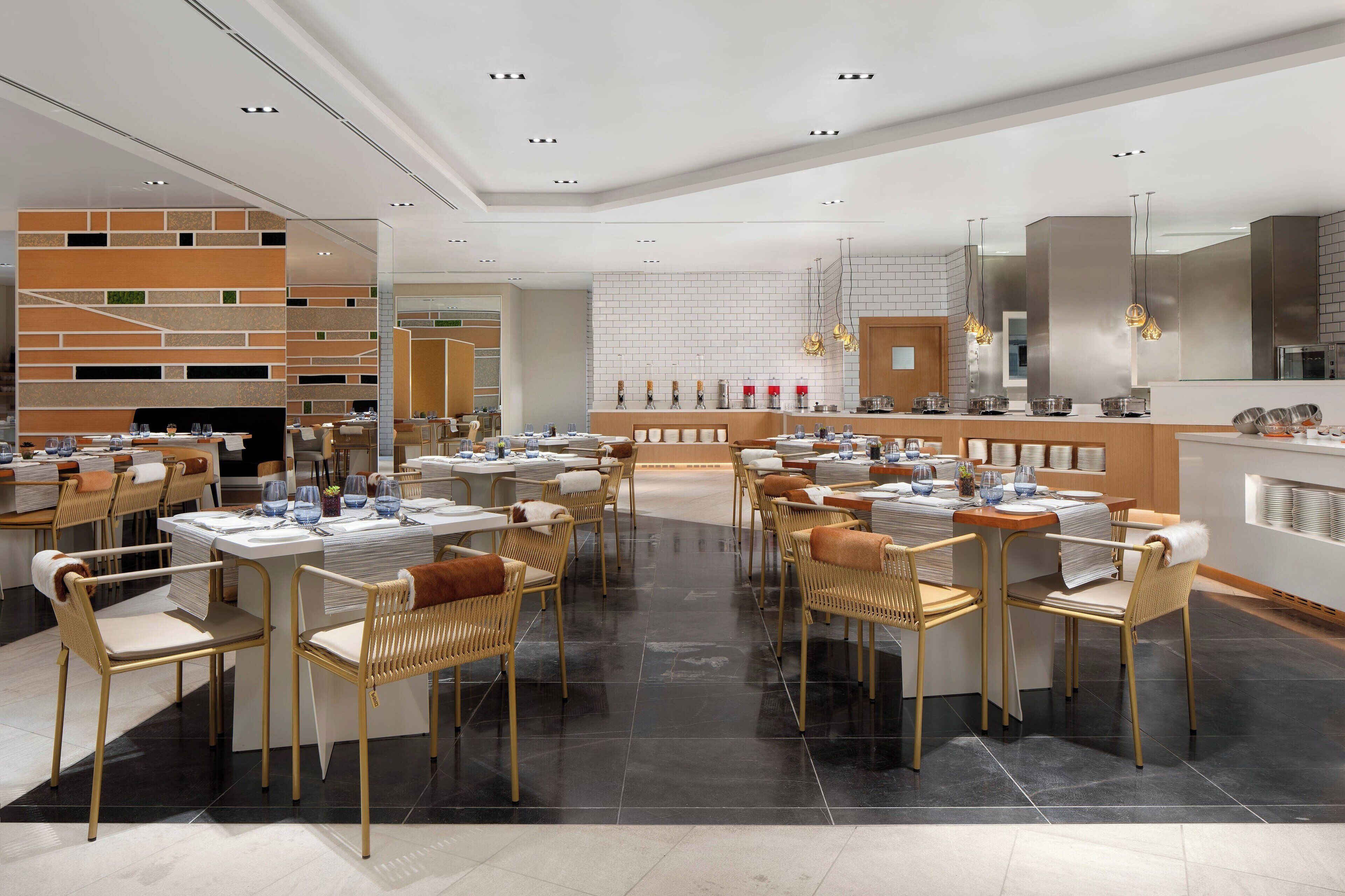 Un restaurant moderne doté de plusieurs tables et chaises, d’un espace cuisine et d’un aménagement propre et contemporain.