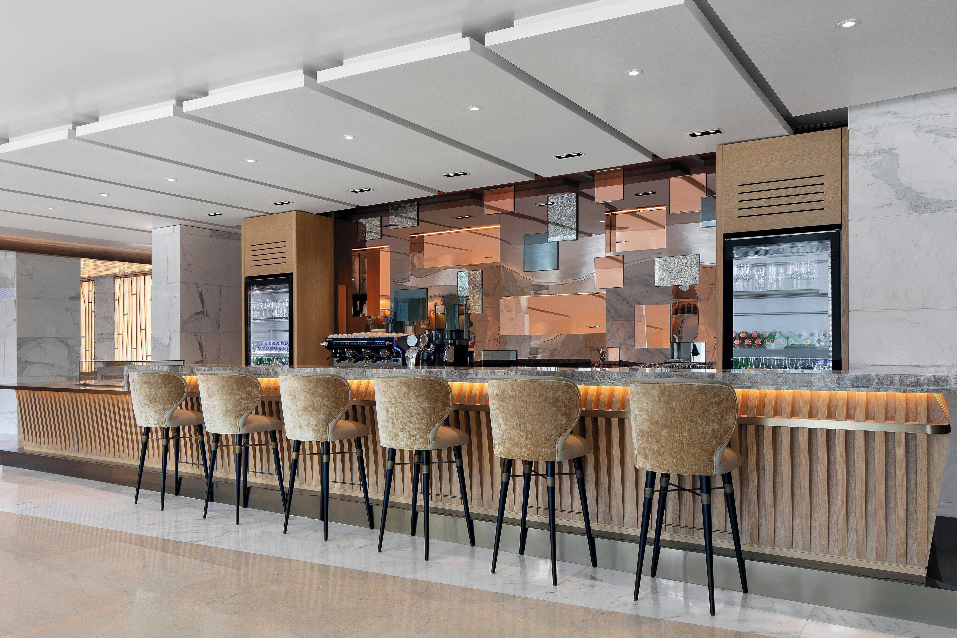 Un espace bar moderne doté d’un long comptoir, de nombreux tabourets et d’un mur décoratif orné de motifs géométriques.