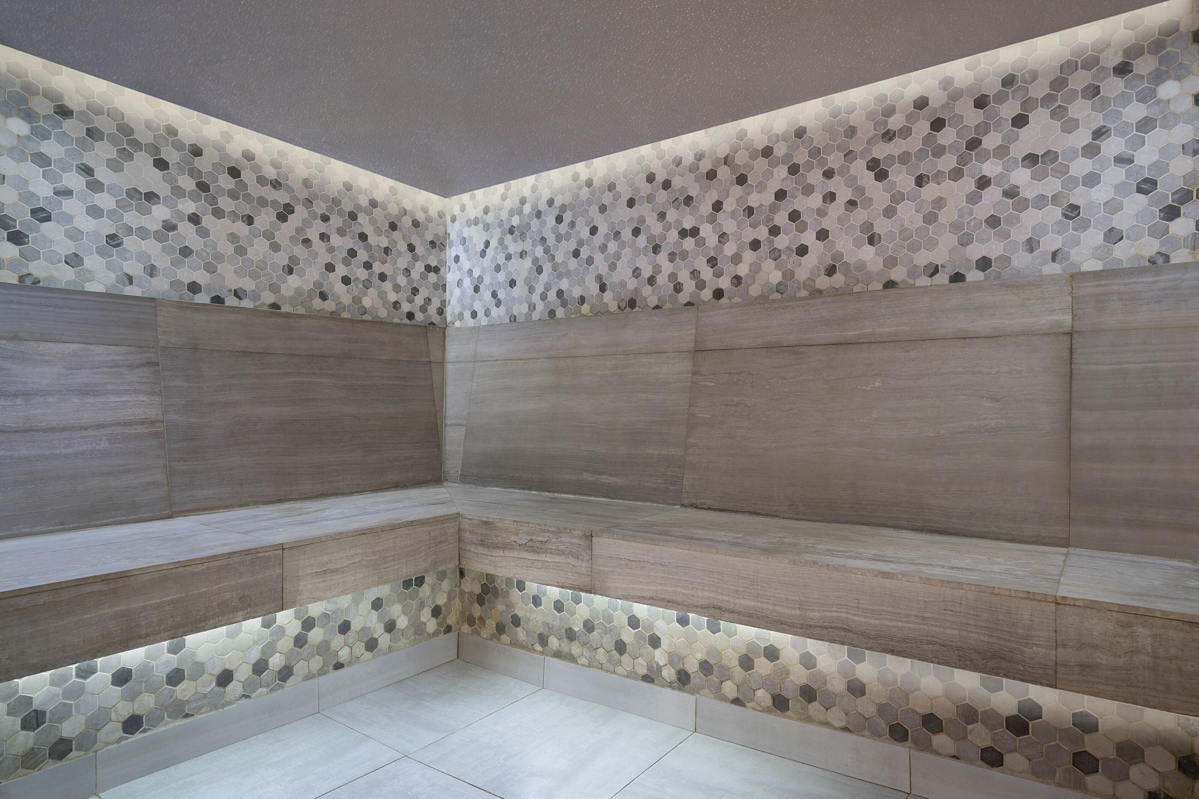 Un coin de pièce dont le bas du mur est orné d’un motif de carreaux hexagonaux et le haut d’un décor en panneaux de bois.