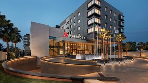 Un hotel Marriott moderno con una fuente curva al frente, palmeras y cielo despejado.