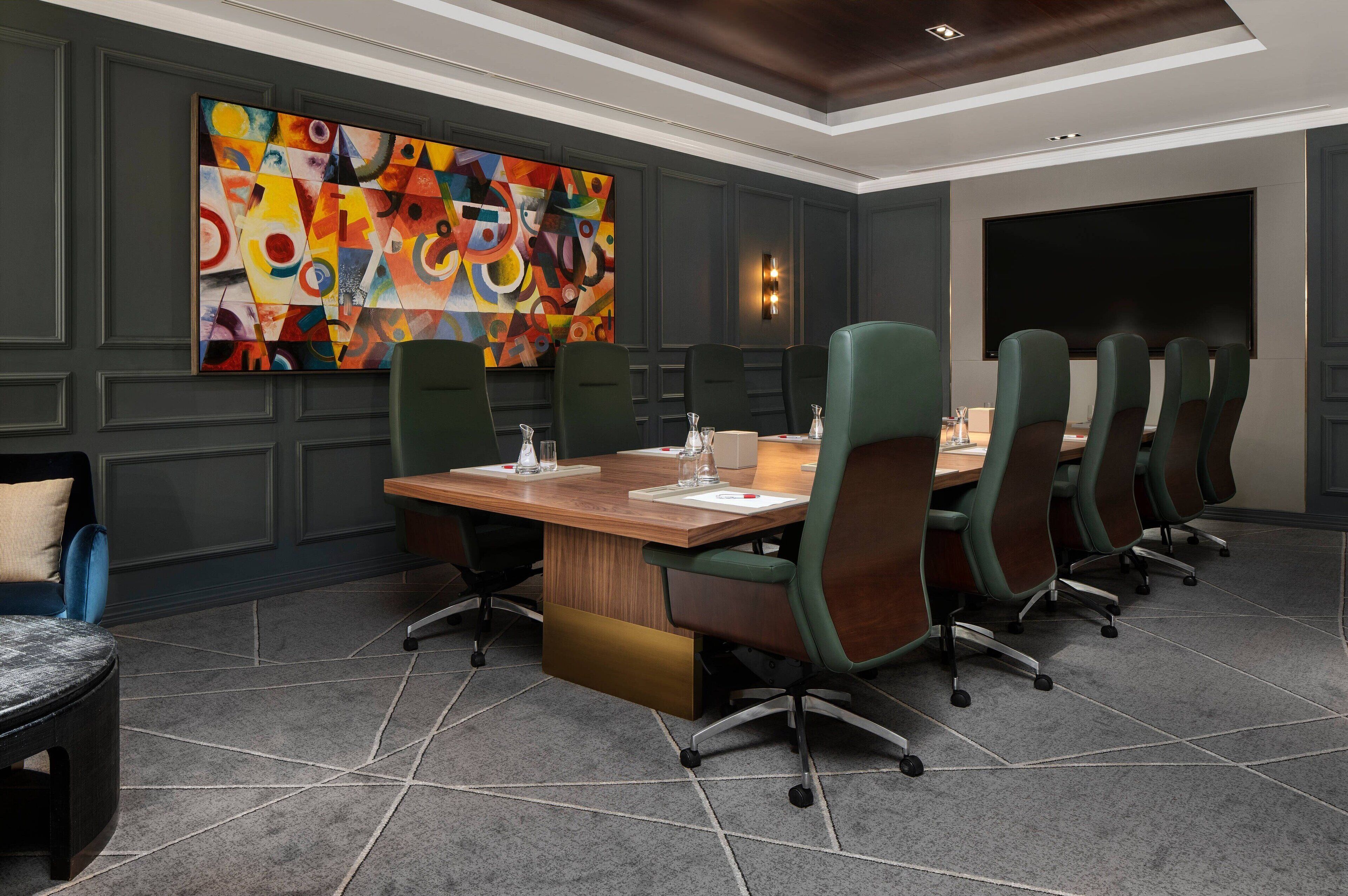 A conference room with a long table, green chairs, and a colorful abstract painting on the wall.