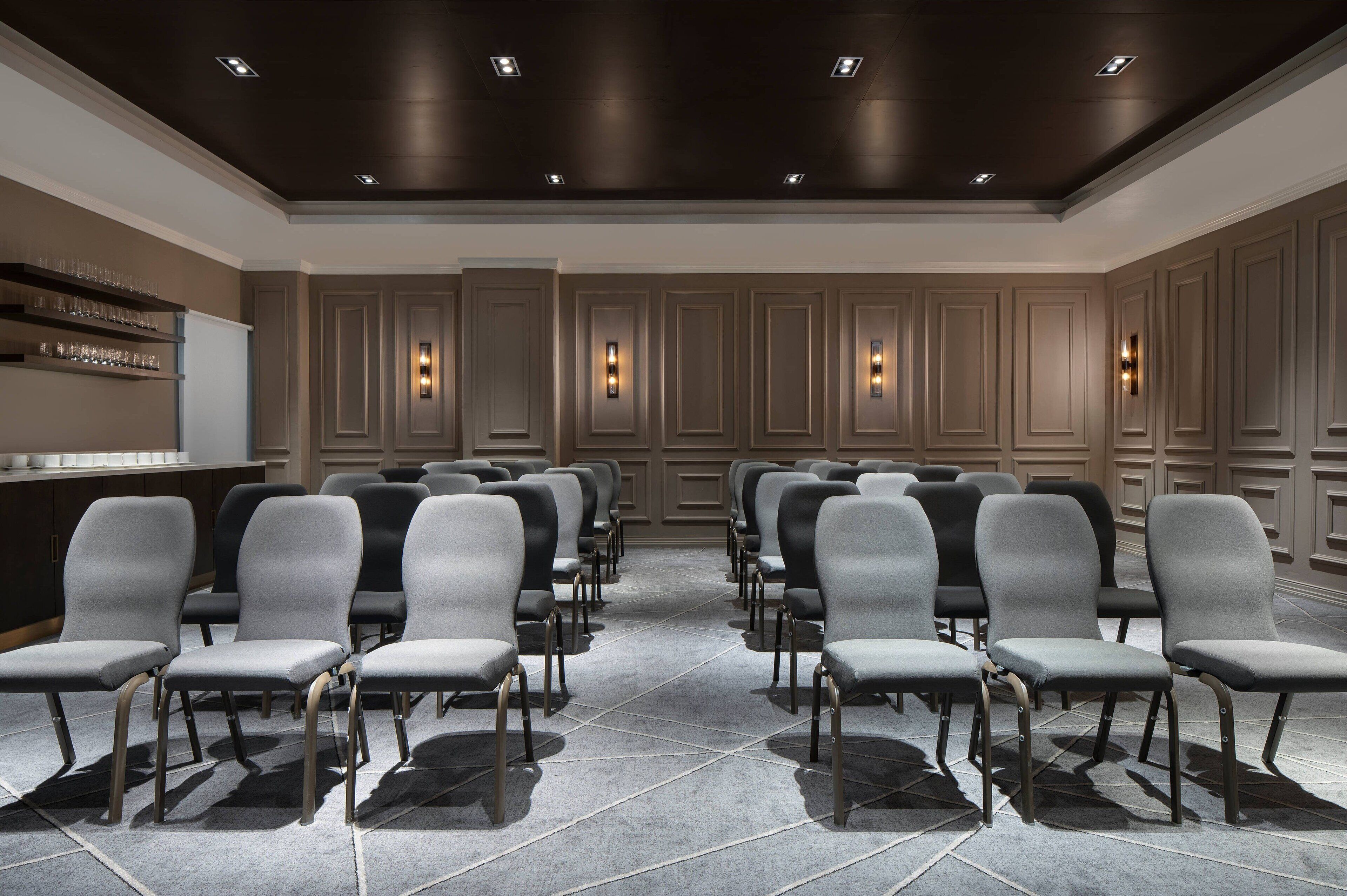 A conference room with rows of grey chairs, a dark ceiling, and wall sconces.