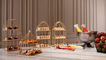 A buffet setup with multiple serving stations, including trays of pastries, sandwiches, and a fruit bowl.