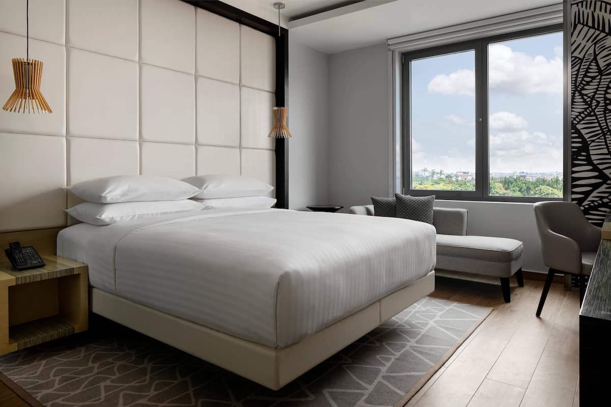 A modern hotel room with a large bed, a desk, and a view of the city.