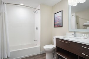 Un baño con bañera, inodoro, tocador con cajones y un espejo grande.