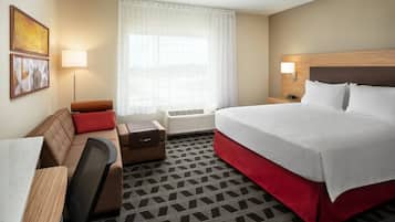 Habitación de hotel con cama, escritorio, silla, sofá, lámpara y ventana con cortinas.