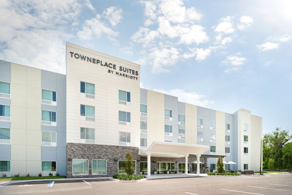 A modern hotel with a sign reading "Towneplace Suites by Marriott". It features a covered entrance, multiple windows, and a parking lot.