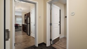 A hotel corridor with a modern kitchen area visible through an open door, including a refrigerator and a dining table.