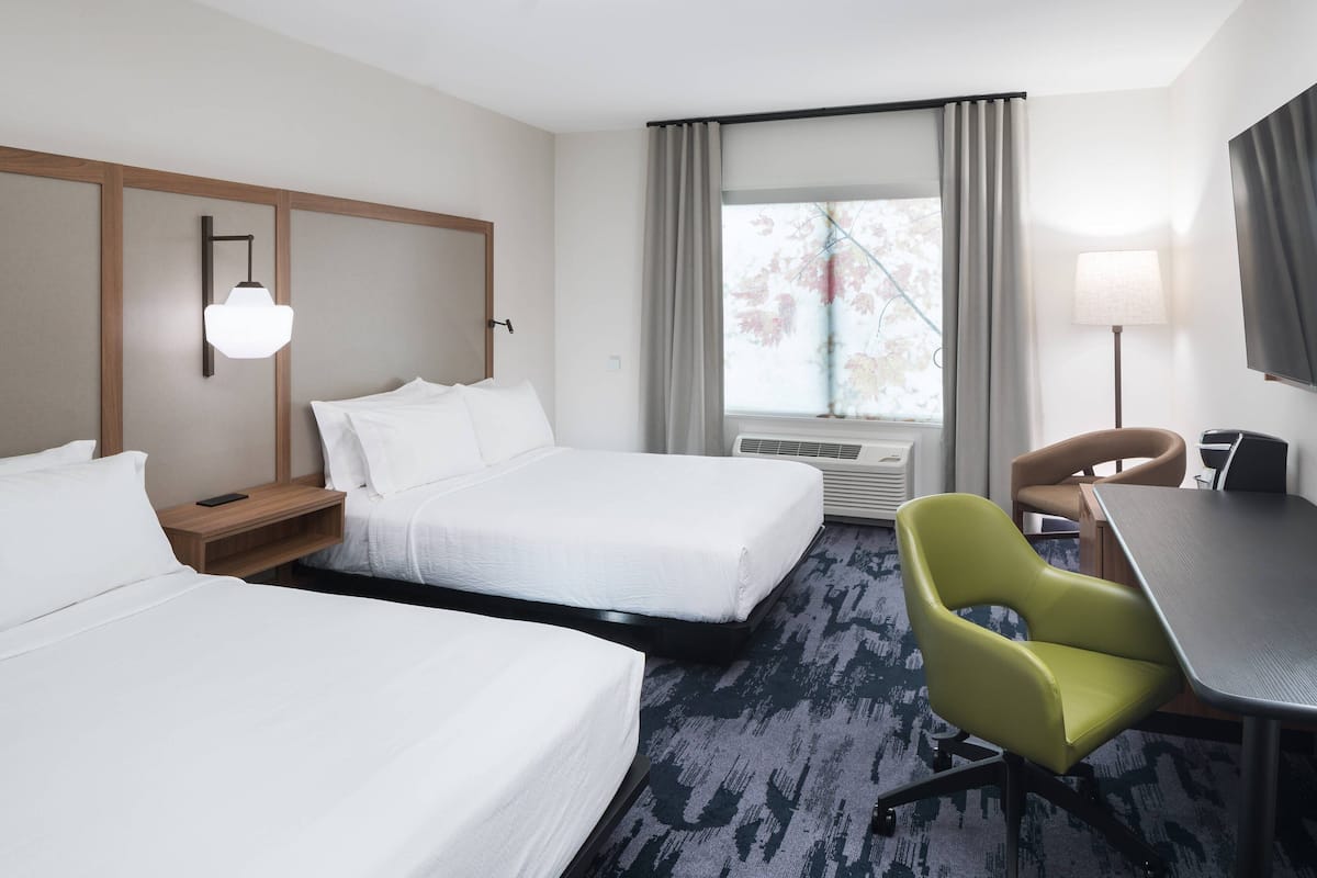 A hotel room with two beds, a desk, a chair, a lamp, and a window with curtains.
