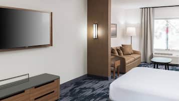 A modern hotel room with a large bed, a flat-screen TV, a wooden cabinet, a sofa, a small table, and a window with curtains.