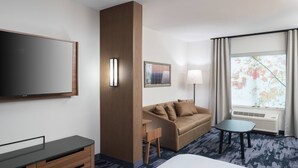 A hotel room with a large bed, a flat-screen TV, a wooden cabinet, a sofa, a small table, and a window with curtains.