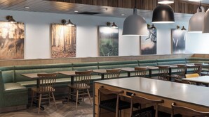 A restaurant with green cushioned booths, wooden tables, and chairs. There are pendant lights above the tables and artwork on the walls.