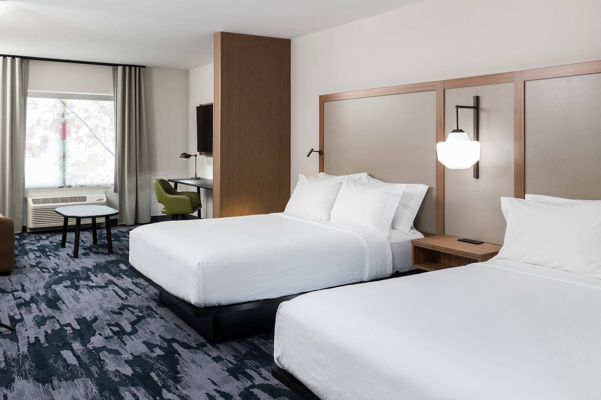 A hotel room with two beds, a desk, a chair, and a window with curtains.