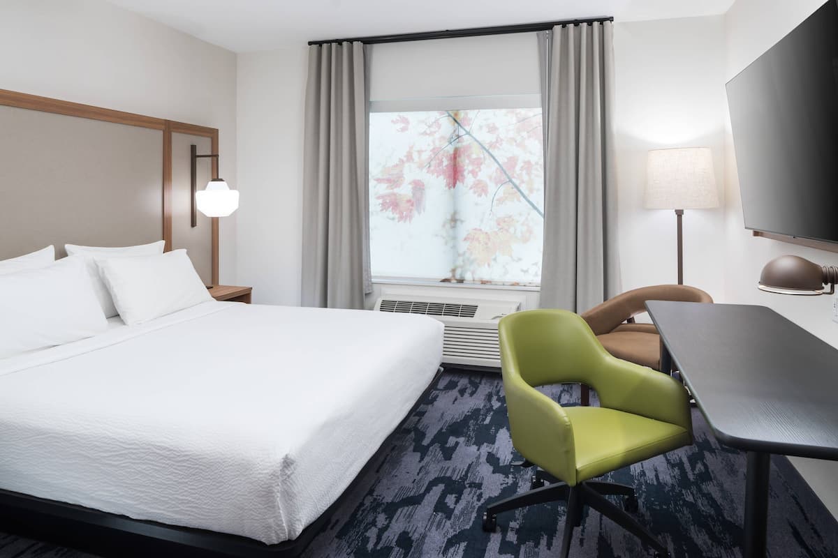 A hotel room with a large bed, a desk, a chair, a TV, and a window with curtains.