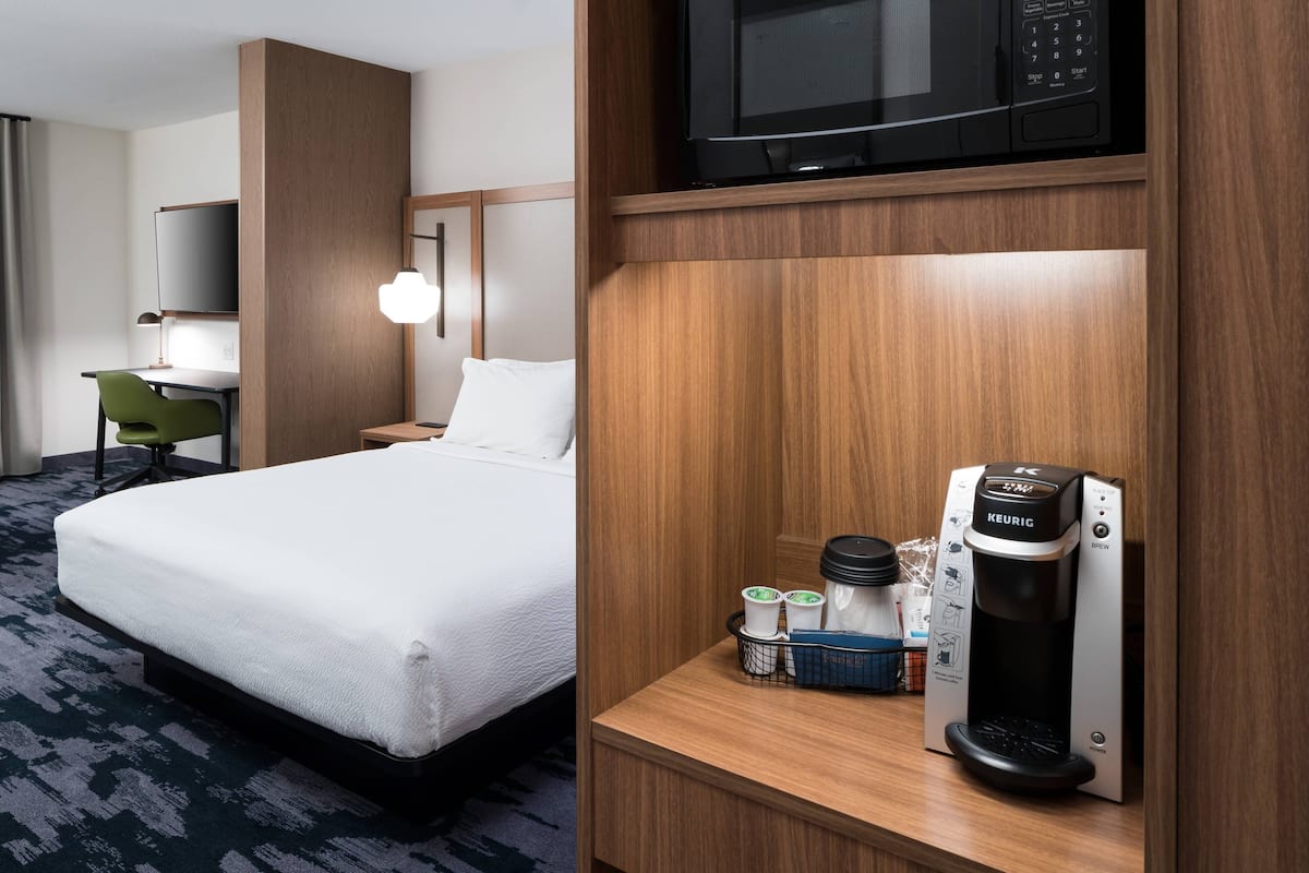 A hotel room with a bed, a desk, a chair, a microwave, and a Keurig coffee machine.