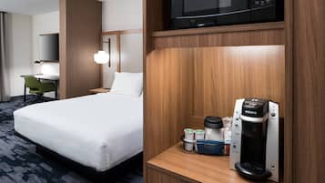 A hotel room with a bed, a desk, a chair, a microwave, and a Keurig coffee machine.