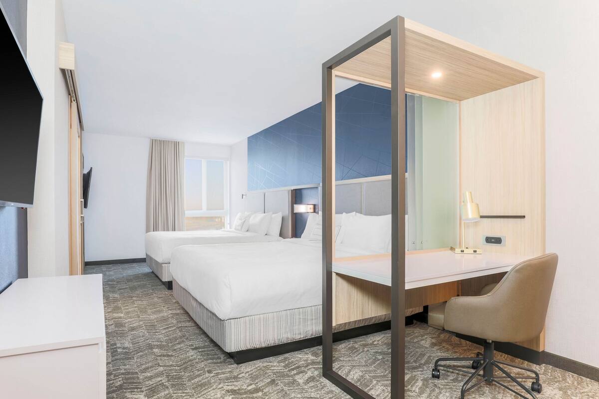A hotel room with two beds, a desk, and a chair.