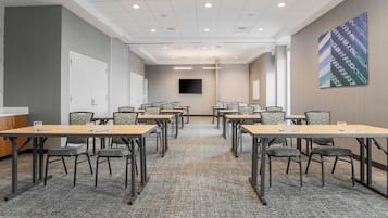 A conference room with multiple tables and chairs, a flat-screen TV mounted on the wall, and a carpeted floor.
